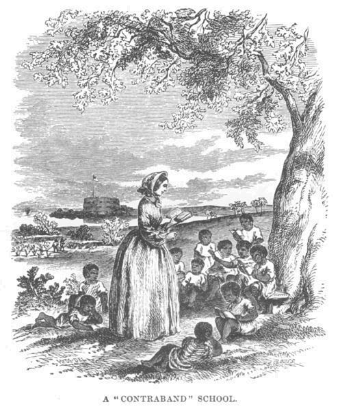 A group of children sit under a tree, a teacher standing in front of them. A fort can be seen in the background.