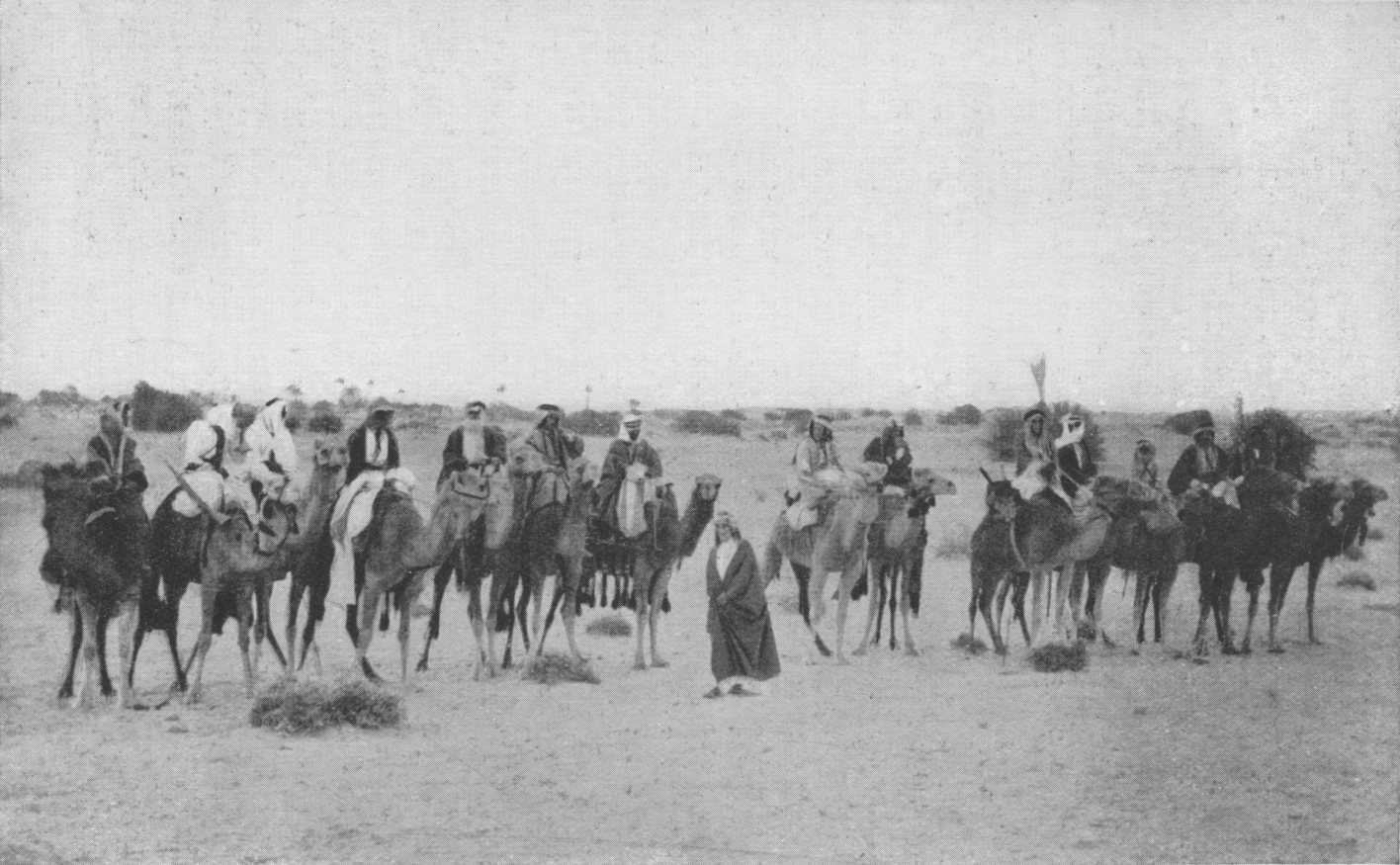 Photo wide shot of Lawrence standing in a line of                 Arabs on camels