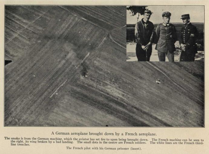 A German aeroplane brought down by a French aeroplane. The smoke is from the German machine, which the aviator has set fire to upon being brought down. The French machine can be seen to the right, its wing broken by a bad landing. The small dots in the center are French soldiers. The white lines are the French third-line trenches. The French pilot with his German prisoner (insert).